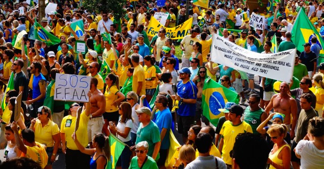 An impeachment protest in Brazil in early 2015. One banner is in English and another protestor is holding up a sign that says S.O.S FFAA, which is a reference to the armed forces (army, military, and navy). The protestors are dressed in Brazilian national colors, a typical feature of the 2015 impeachment protests.