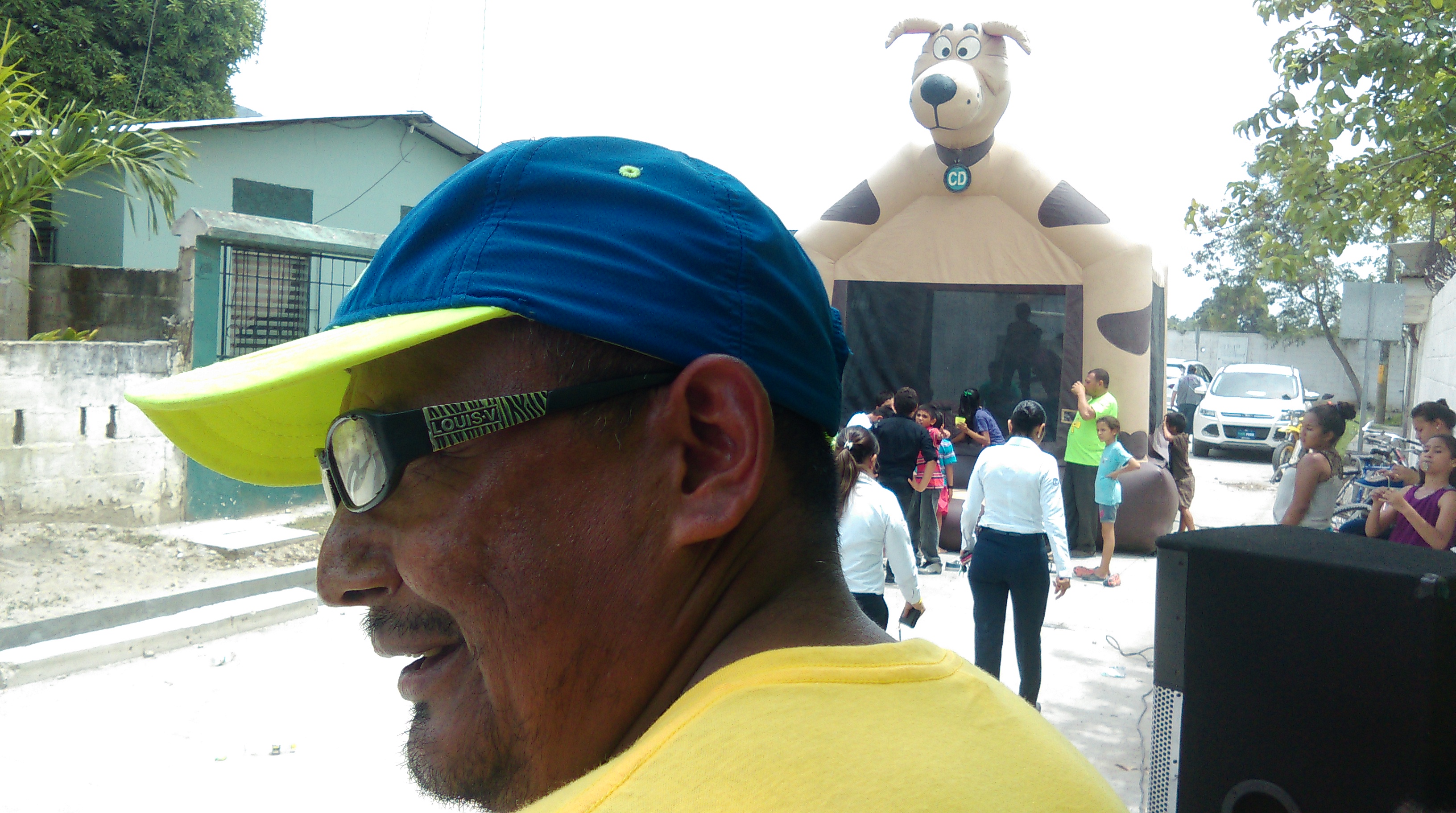 Photo of a man in glasses, behind him there's children in line waiting to go inside a jumper