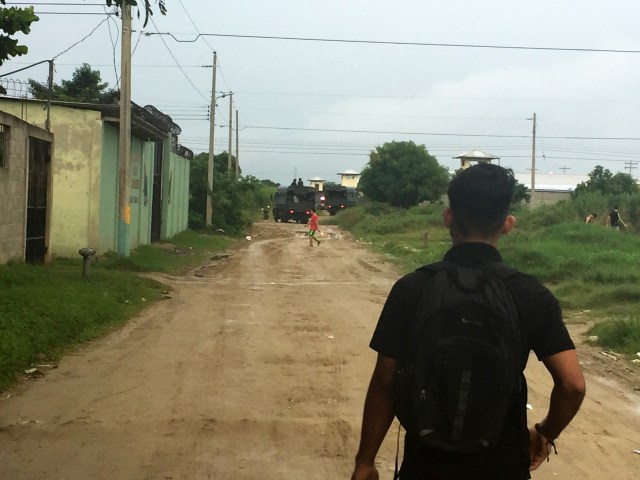 Image of a boy walking down a trail with military trucks returning from patrols at the end of the trail.