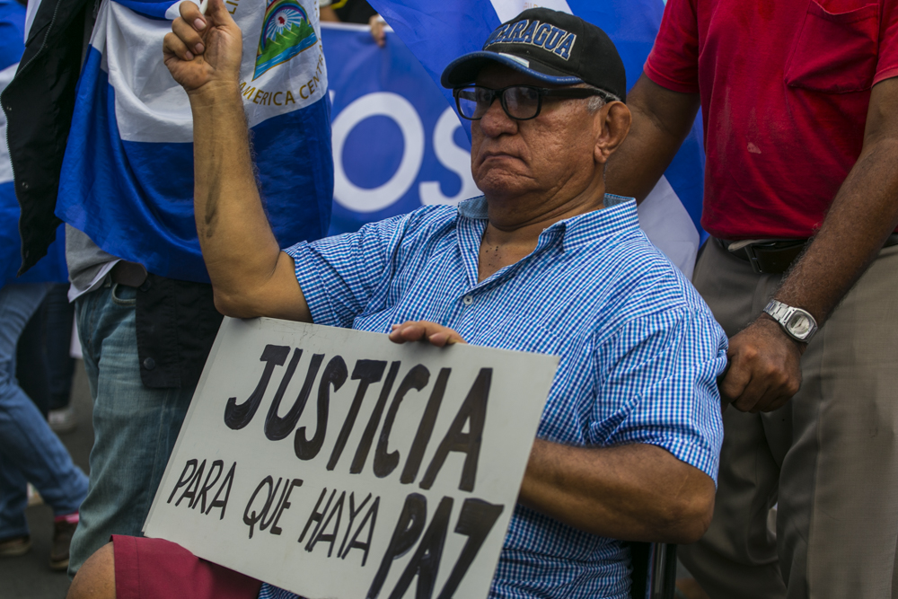 A citizen holding up a sign  at a demonstration that says "Justice so there may be peace"