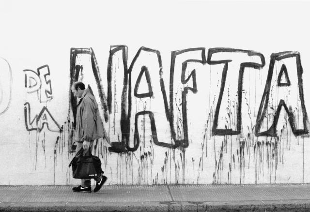 A man in Nikes walks in Buenos Aires in front of "NAFTA" graffiti.