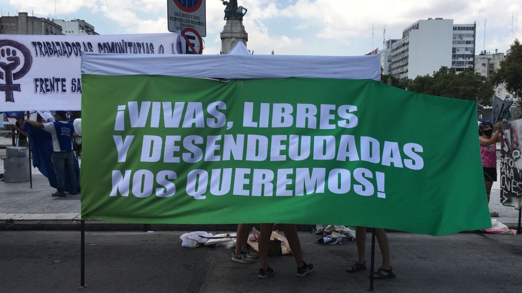 Foto de la manifestación por el 8 de marzo en Buenos Aires, 2021. Un grupo de manifestantes muestra una gran bandera verde que dice "¡Vivas, libres y desendeudadas nos queremos!". (Foto de Sofia Besandon.)