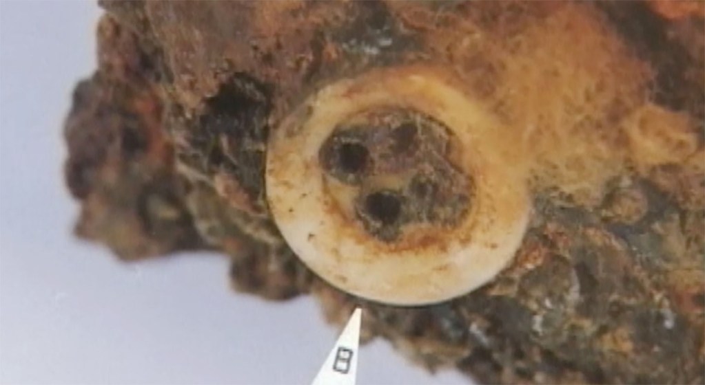 Close up of a pearl button still attached to a piece of steel railroad track. (Image from The Judge and the General.)