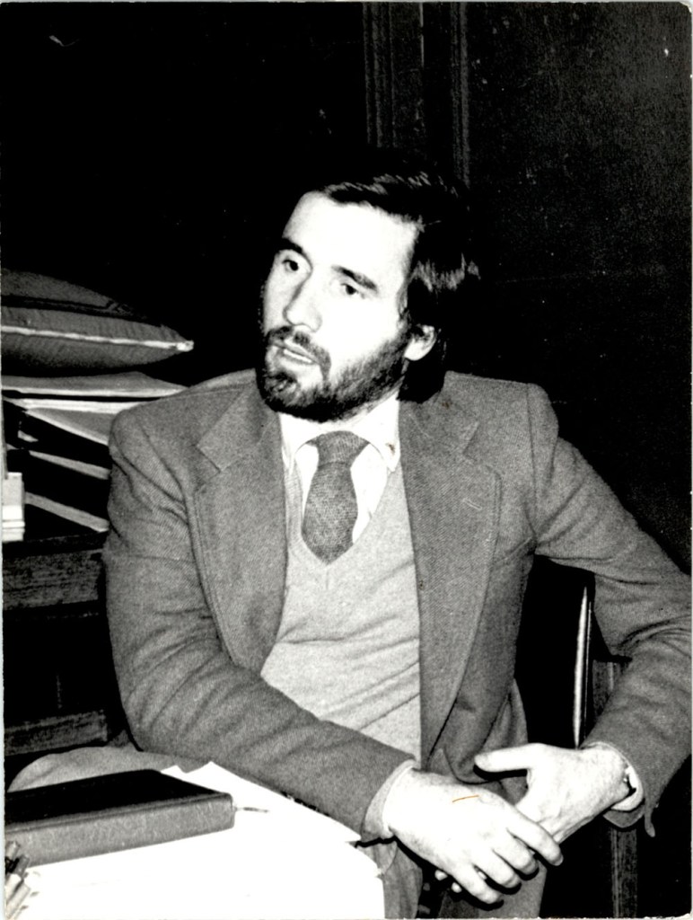 Álvaro Varela in this black and white 1975 photo wears a jacket and tie and listens to a question.