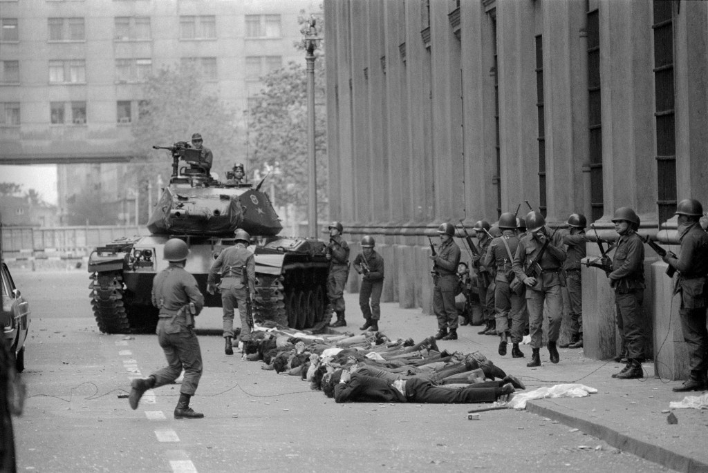 Soldados y un tanque custodian a un grupo de detenidos tirados en la calle con las manos entrelazadas detrás de la cabeza.