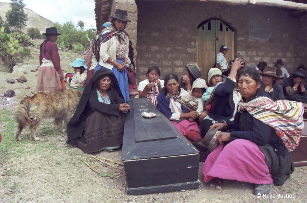 Crying women and children surround a black casket lying on the ground.