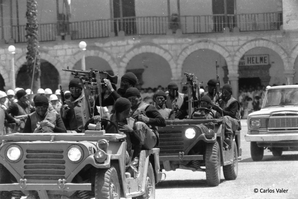 Soldiers in jeeps armed with machine guns traverse a public square.