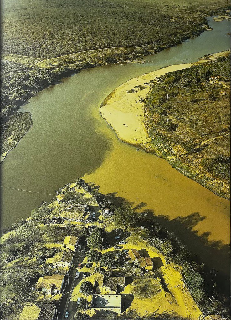 An aerial photograph of the joining of two rivers, with a small village in the foreground between them.
