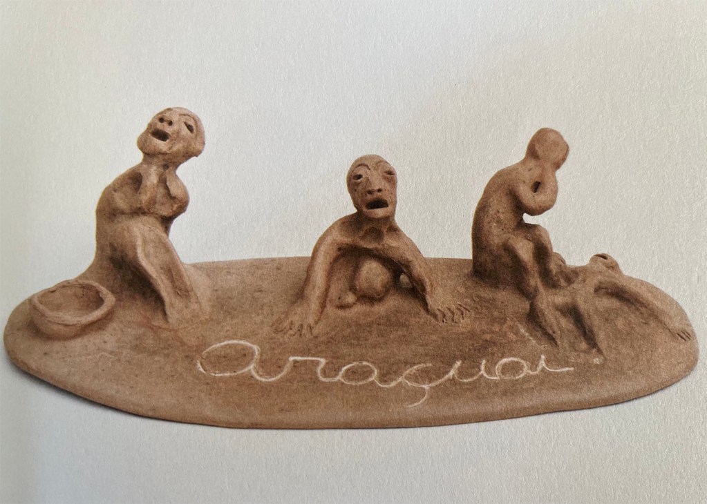 A ceramic sculpture of three figures mourning a fourth laying on the ground, with the name Araçuaí inset into the base.