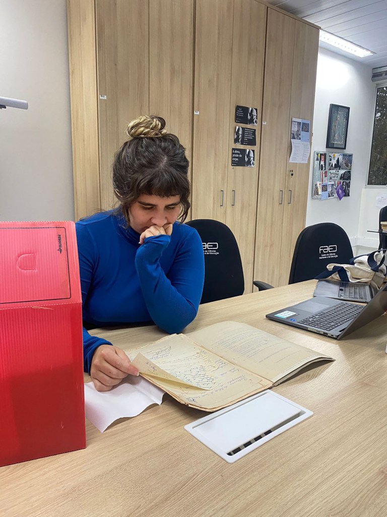 The author sits with her laptop reading documents on a table.