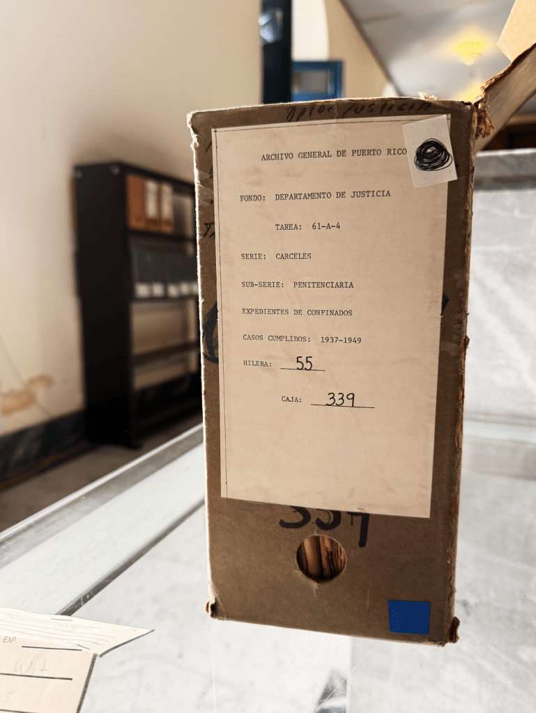 A cardboard box labeled 'Archivo General de Puerto Rico' containing information about penitentiary records, with details about file organization and historical context.