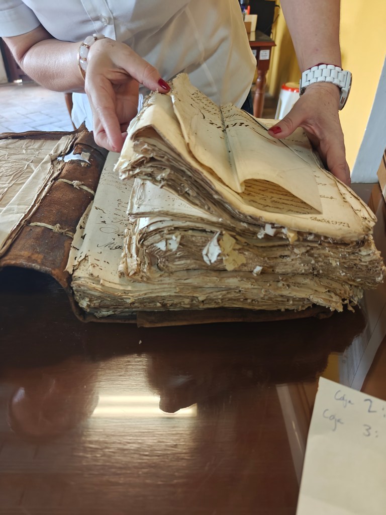A person is holding a stack of antique books with yellowed pages, showing signs of wear and tear, on a wooden table.