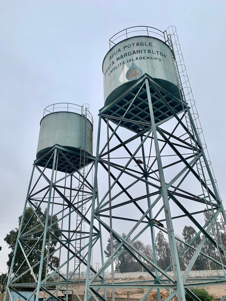 Two water tanks labeled 'Agua Potable Santa Margarita Alta' on metal structures, surrounded by trees and a cloudy sky.